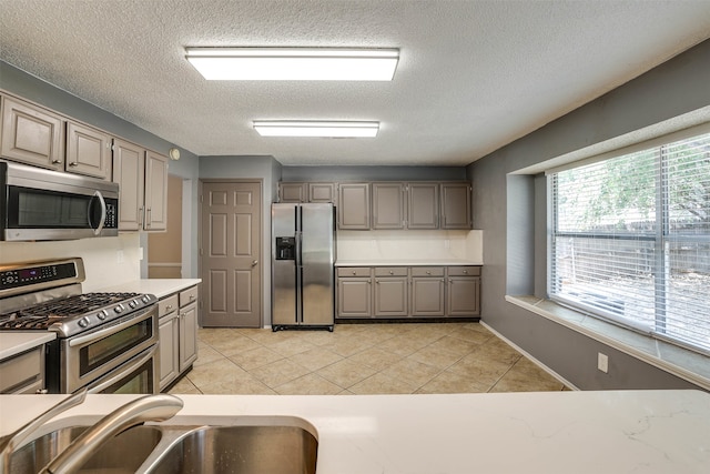 kitchen with appliances with stainless steel finishes, light tile patterned flooring, a textured ceiling, and sink