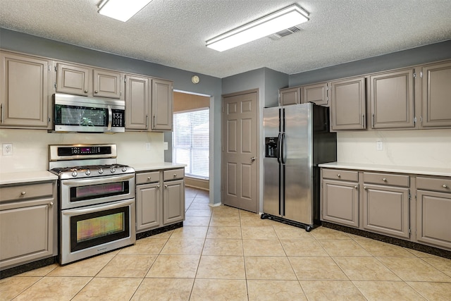 kitchen with gray cabinets, appliances with stainless steel finishes, a textured ceiling, and light tile patterned floors