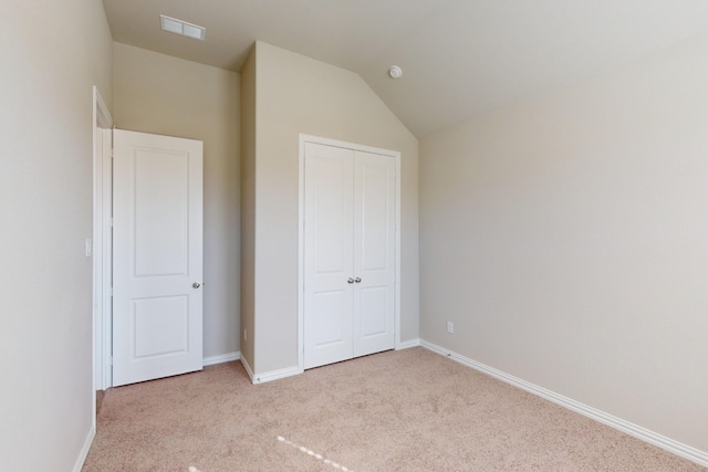 unfurnished bedroom with light carpet, a closet, and lofted ceiling