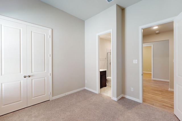 unfurnished bedroom with light colored carpet, ensuite bath, and a closet