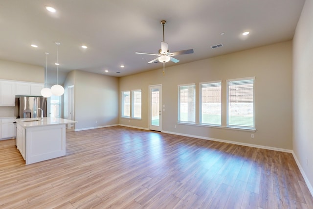 kitchen with white cabinets, stainless steel fridge with ice dispenser, light hardwood / wood-style floors, and a kitchen island with sink