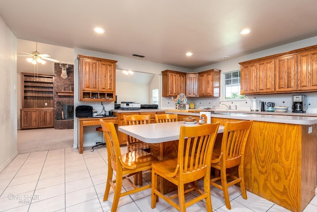 kitchen with ceiling fan, a brick fireplace, brick wall, light carpet, and a kitchen bar