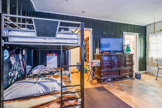 bedroom with a textured ceiling, parquet floors, and wood walls