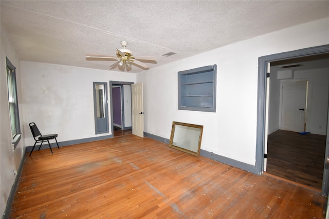 spare room featuring built in features, a textured ceiling, ceiling fan, and hardwood / wood-style floors