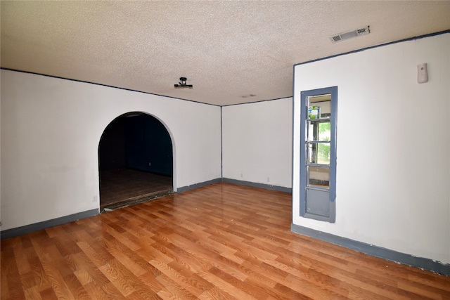 empty room with light wood-type flooring and a textured ceiling