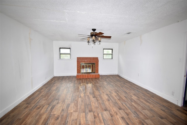 unfurnished living room featuring a textured ceiling, a brick fireplace, dark hardwood / wood-style flooring, and ceiling fan