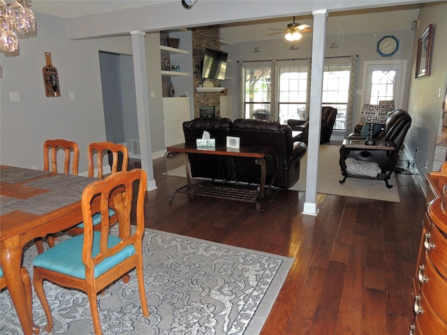 dining space featuring built in shelves, ceiling fan, ornate columns, dark hardwood / wood-style floors, and a fireplace