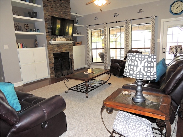 living room with built in shelves, ceiling fan, and a stone fireplace