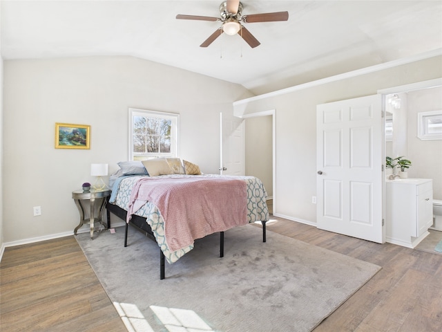 bedroom featuring vaulted ceiling, ensuite bathroom, baseboards, and wood finished floors