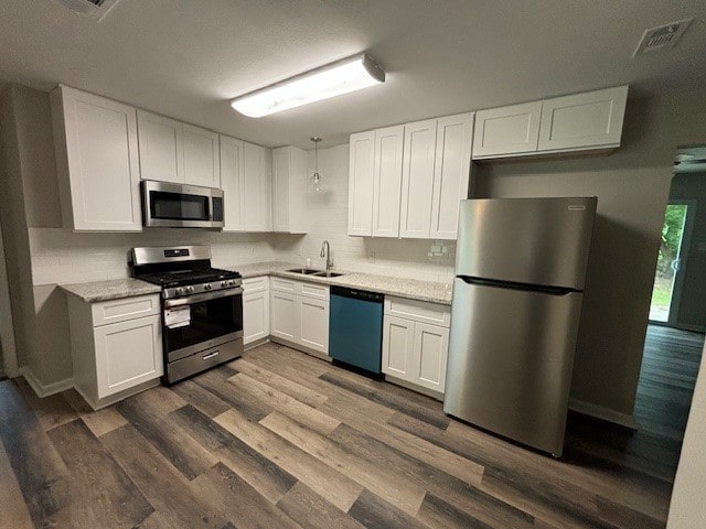 kitchen with appliances with stainless steel finishes, sink, light stone counters, white cabinetry, and dark wood-type flooring