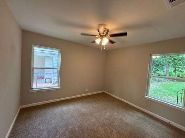 carpeted empty room featuring a ceiling fan, visible vents, and baseboards