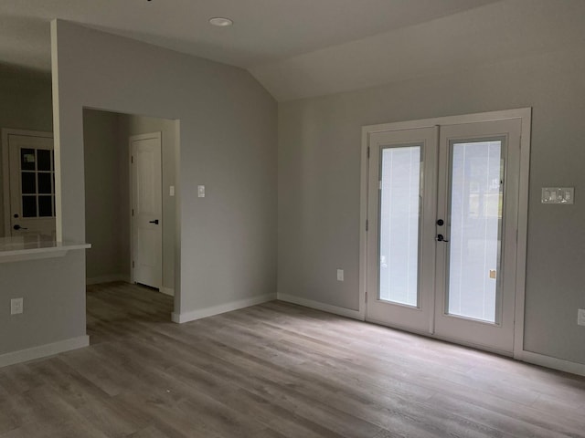 unfurnished room featuring a healthy amount of sunlight, light hardwood / wood-style floors, vaulted ceiling, and french doors