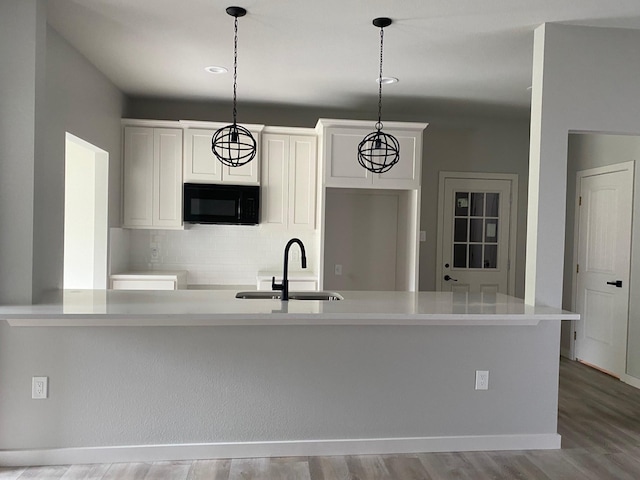 kitchen with hanging light fixtures, sink, white cabinets, light wood-type flooring, and backsplash