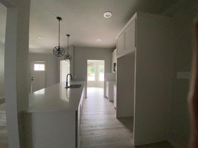 kitchen featuring sink, decorative light fixtures, white cabinets, light wood-type flooring, and a kitchen island with sink