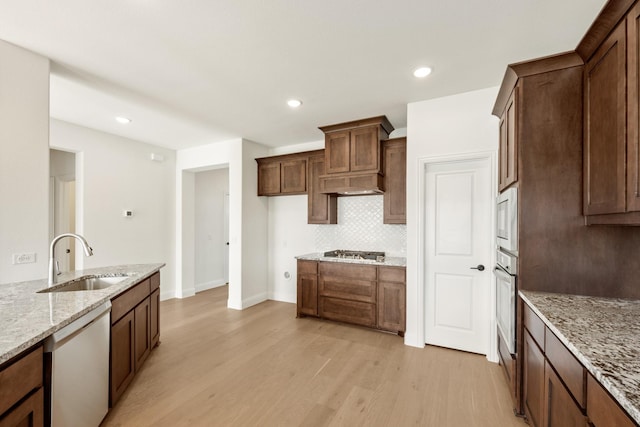 kitchen with sink, stainless steel appliances, tasteful backsplash, light stone counters, and light hardwood / wood-style flooring