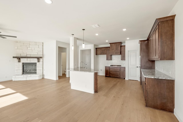 kitchen featuring decorative backsplash, light stone countertops, hanging light fixtures, and light hardwood / wood-style flooring