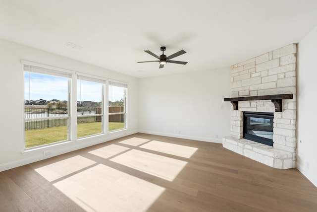 unfurnished living room with a fireplace, hardwood / wood-style floors, a water view, and ceiling fan