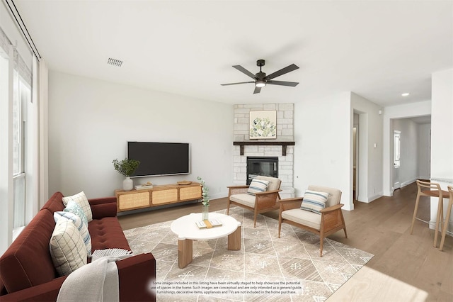 living room featuring ceiling fan, a stone fireplace, and wood-type flooring