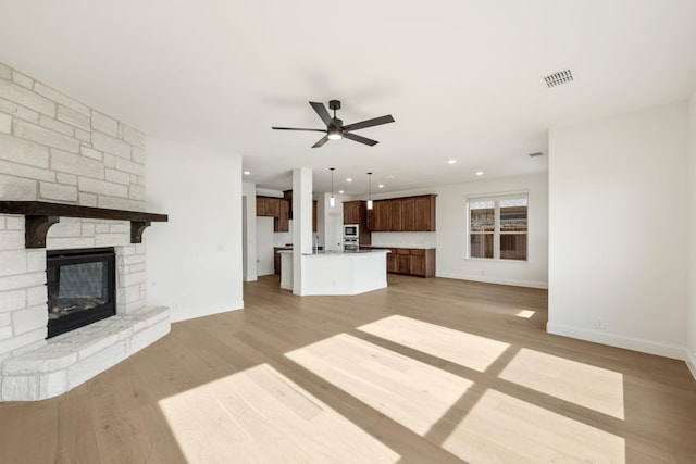 unfurnished living room with light wood-type flooring, a stone fireplace, and ceiling fan