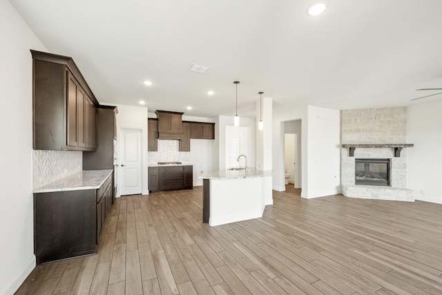 kitchen with decorative backsplash, light stone counters, light hardwood / wood-style flooring, and hanging light fixtures