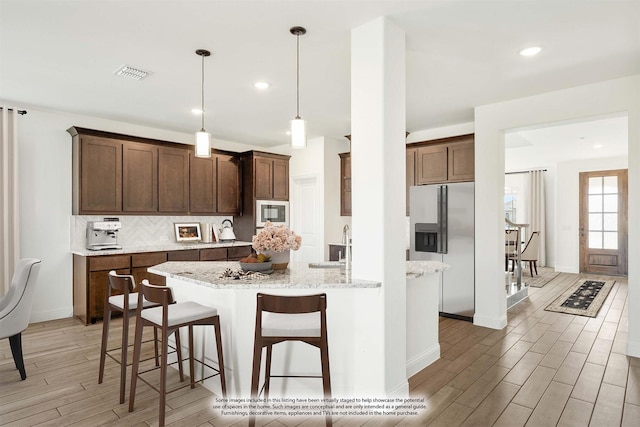 kitchen featuring decorative backsplash, built in microwave, decorative light fixtures, light stone counters, and stainless steel fridge with ice dispenser