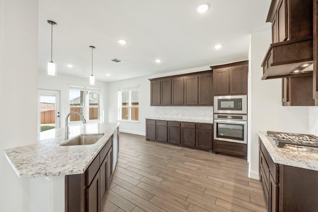 kitchen featuring light stone countertops, stainless steel appliances, sink, decorative light fixtures, and light hardwood / wood-style floors