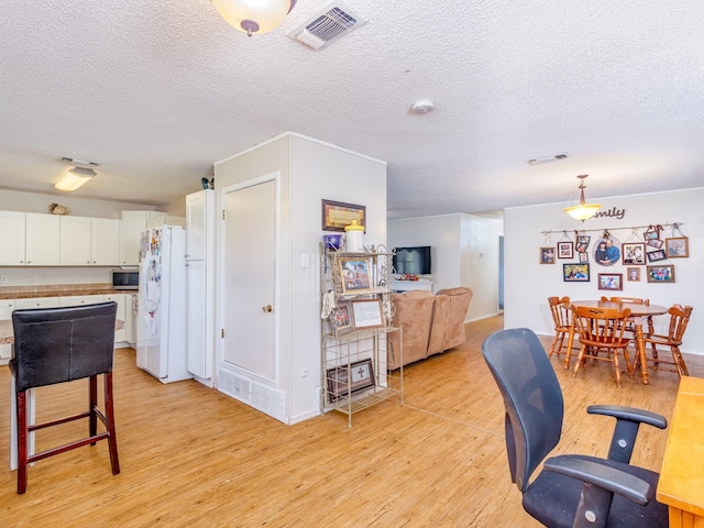 kitchen featuring a textured ceiling, white fridge, white cabinets, light wood-type flooring, and pendant lighting