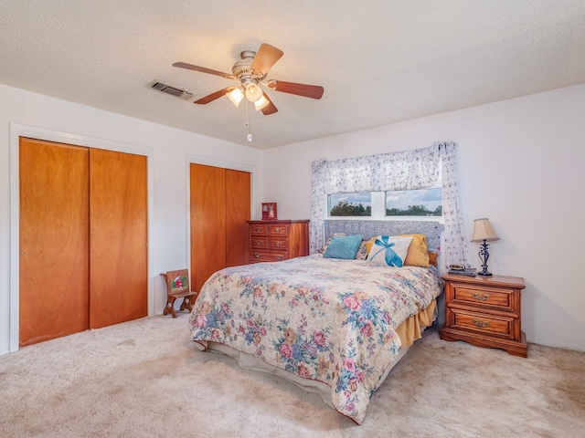 carpeted bedroom featuring multiple closets, ceiling fan, and a textured ceiling