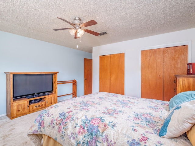 carpeted bedroom with multiple closets, a textured ceiling, and ceiling fan