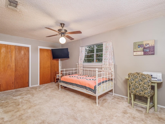 carpeted bedroom with ceiling fan, two closets, and a textured ceiling