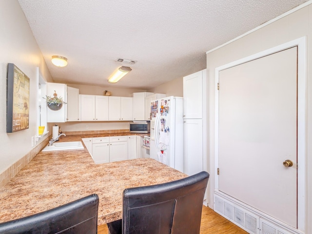 kitchen with white fridge with ice dispenser, white cabinetry, a textured ceiling, and sink