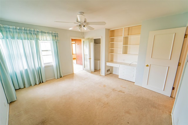 unfurnished bedroom featuring ceiling fan, light colored carpet, and built in desk