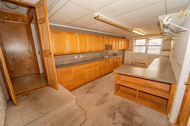 kitchen featuring sink, decorative light fixtures, light colored carpet, brick wall, and a drop ceiling