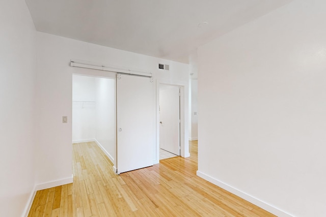 unfurnished bedroom featuring a barn door, a closet, and light hardwood / wood-style floors