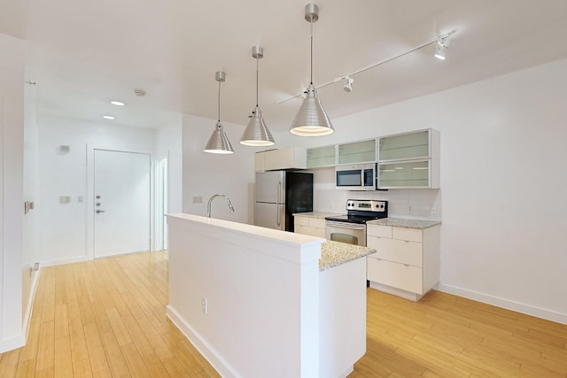 kitchen with white cabinets, backsplash, light wood-type flooring, stainless steel appliances, and an island with sink