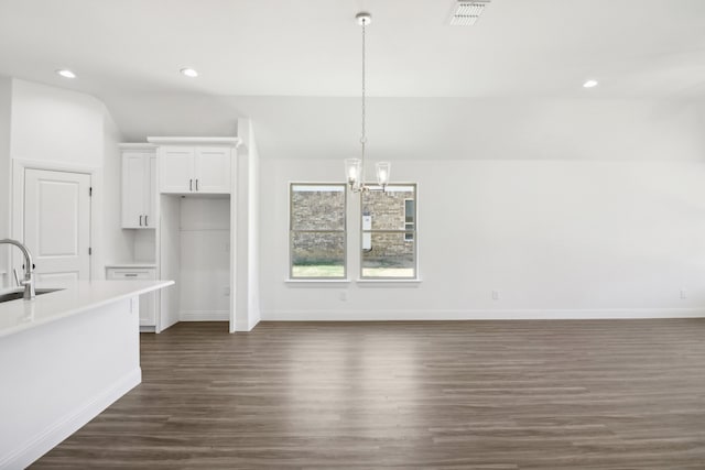 kitchen with white cabinets, pendant lighting, sink, dark wood-type flooring, and an inviting chandelier