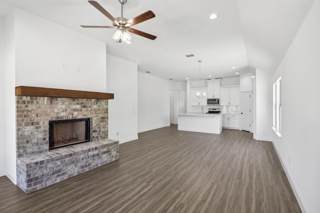 unfurnished living room with ceiling fan, vaulted ceiling, a fireplace, and dark wood-type flooring