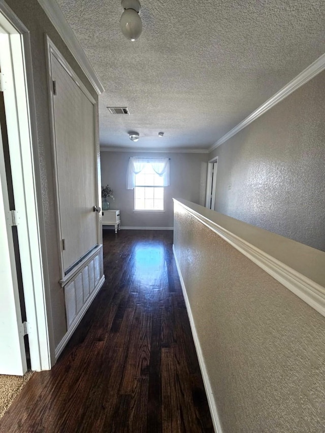 corridor featuring visible vents, dark wood-style flooring, crown molding, and a textured wall