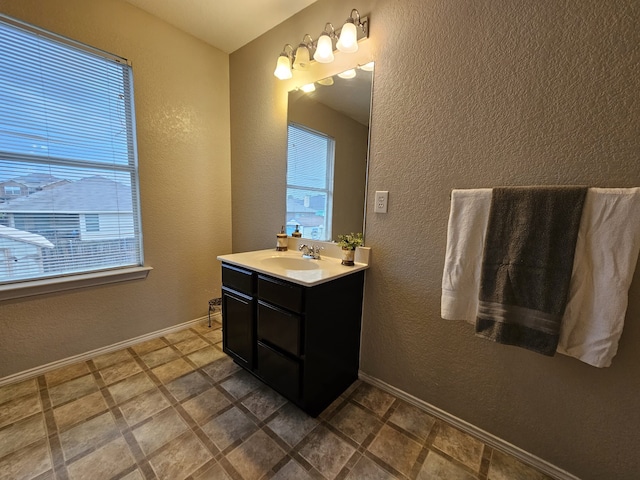 bathroom with a healthy amount of sunlight, vanity, baseboards, and a textured wall