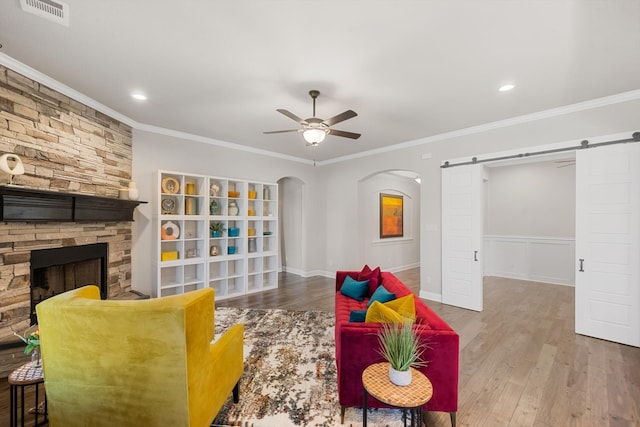 living room with hardwood / wood-style floors, a barn door, a stone fireplace, and crown molding