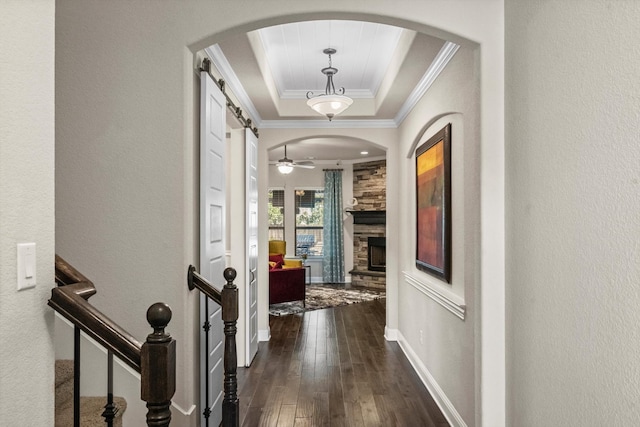 corridor with a barn door, a raised ceiling, dark wood-type flooring, and crown molding