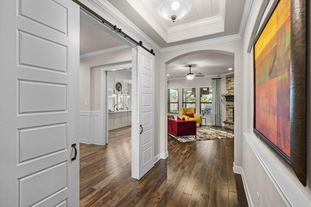 hallway with a barn door, ornamental molding, dark wood-type flooring, and a tray ceiling