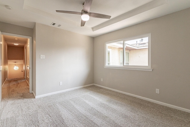 spare room with ceiling fan, a tray ceiling, and carpet