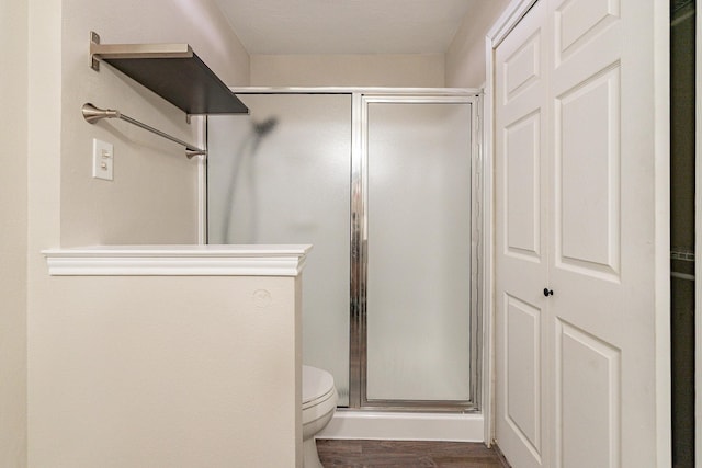 bathroom with toilet, a shower with door, and wood-type flooring