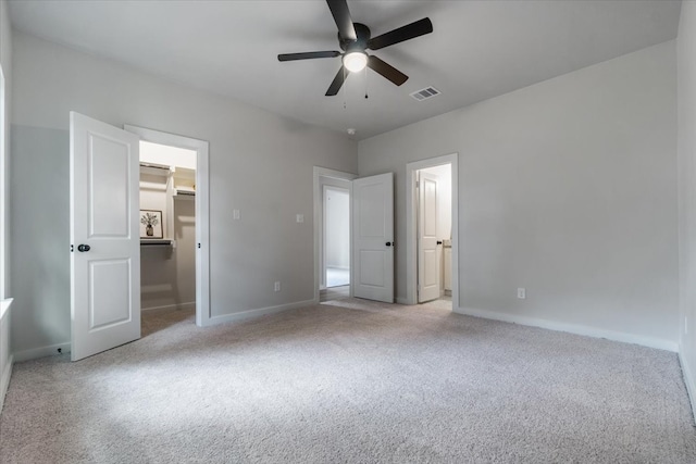 unfurnished bedroom with light carpet, ceiling fan, and a walk in closet