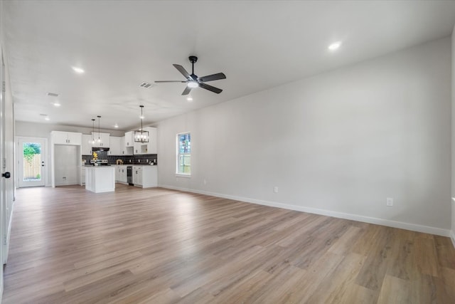 unfurnished living room with ceiling fan with notable chandelier and light hardwood / wood-style floors