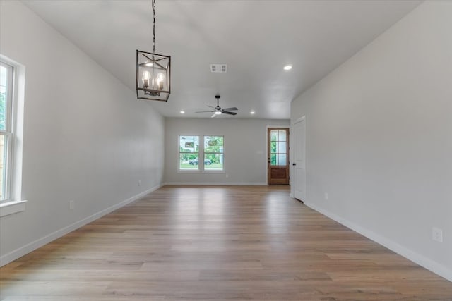 spare room with ceiling fan with notable chandelier and light wood-type flooring