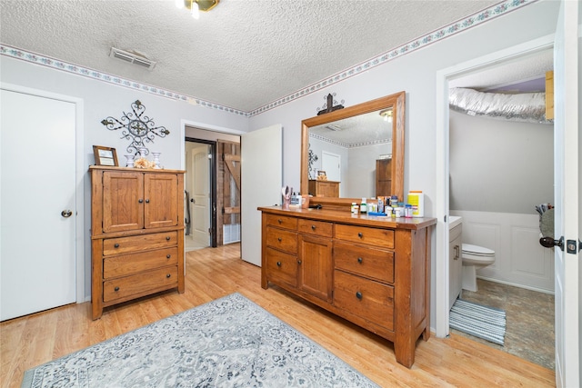 bedroom with ensuite bath, light wood-type flooring, and a textured ceiling