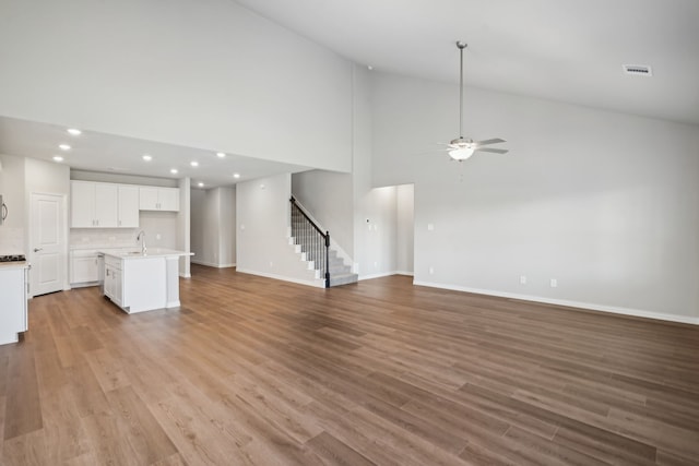 unfurnished living room featuring ceiling fan, light wood-type flooring, sink, and high vaulted ceiling