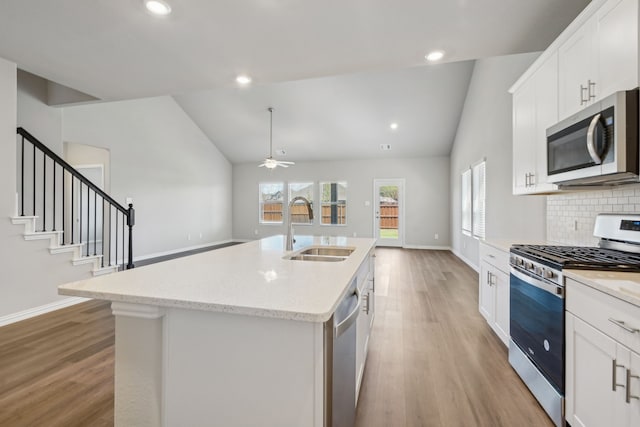 kitchen with lofted ceiling, an island with sink, appliances with stainless steel finishes, and sink